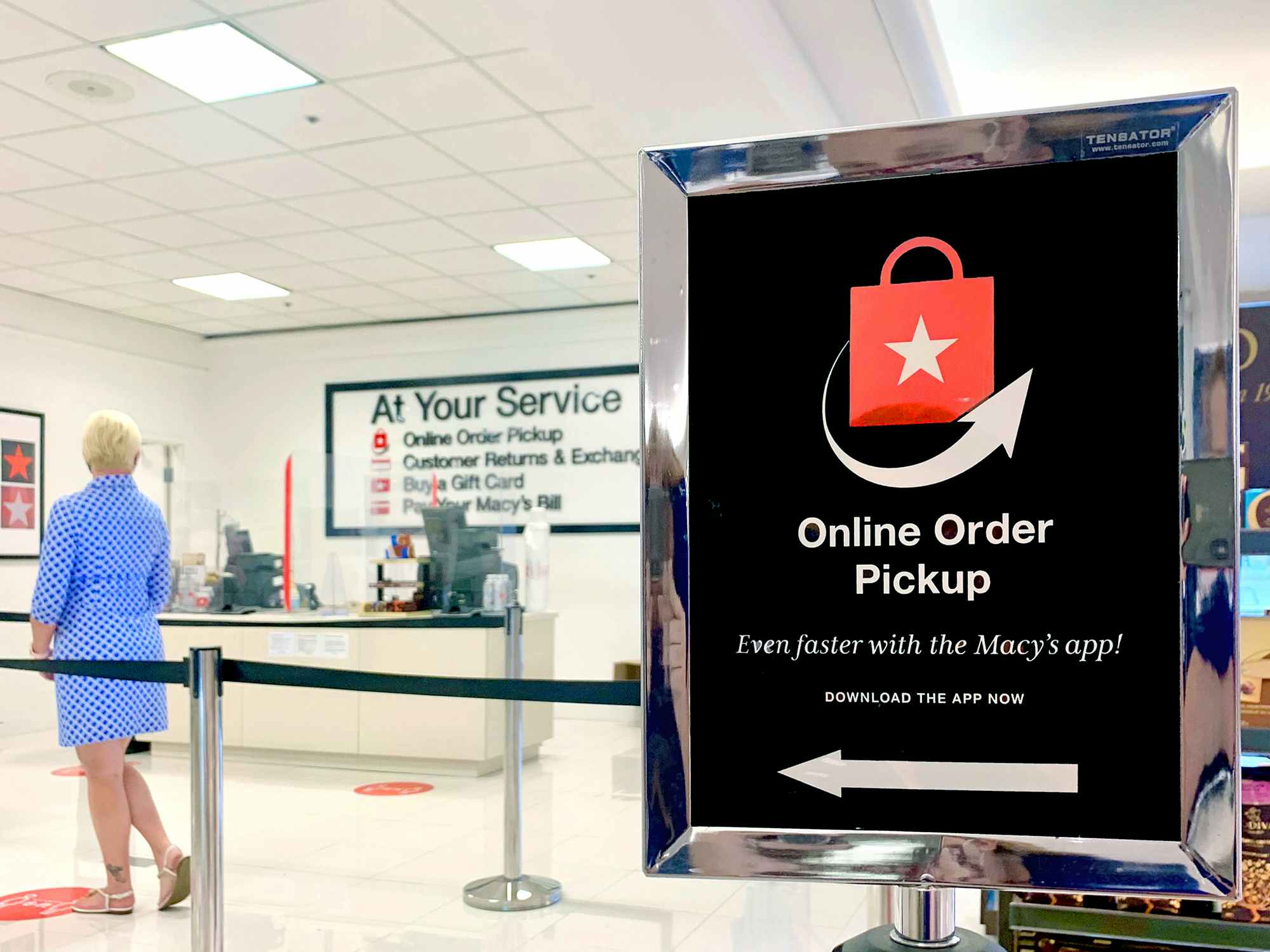 A Macy's Online Order Pickup sign pointing to a roped area where a person is standing in line for the Macy's service desk.