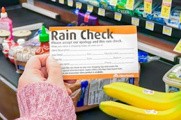A person's hand holding a rain check card over a conveyer belt stacked with groceries at Albertson's.