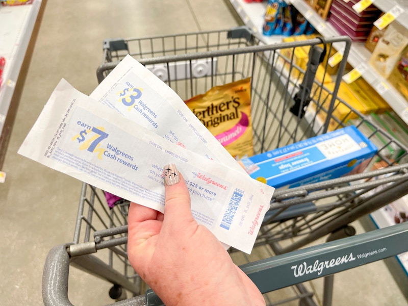 someone holding Walgreens cash rewards in front of a cart in walgreens