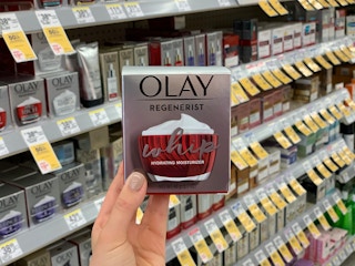 A hand holding a container of Olay Regenerist Whip Face Cream.