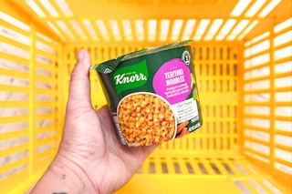 hand holding a knorr pasta cup above a yellow shopping basket