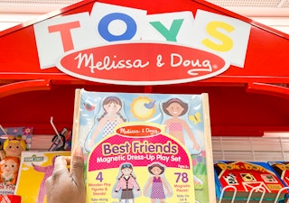 A person holding up a Melissa & Doug toy under a display for the brand.