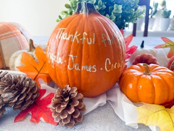 thankful message and names written in metallic pen on a pumpkin sitting on a table