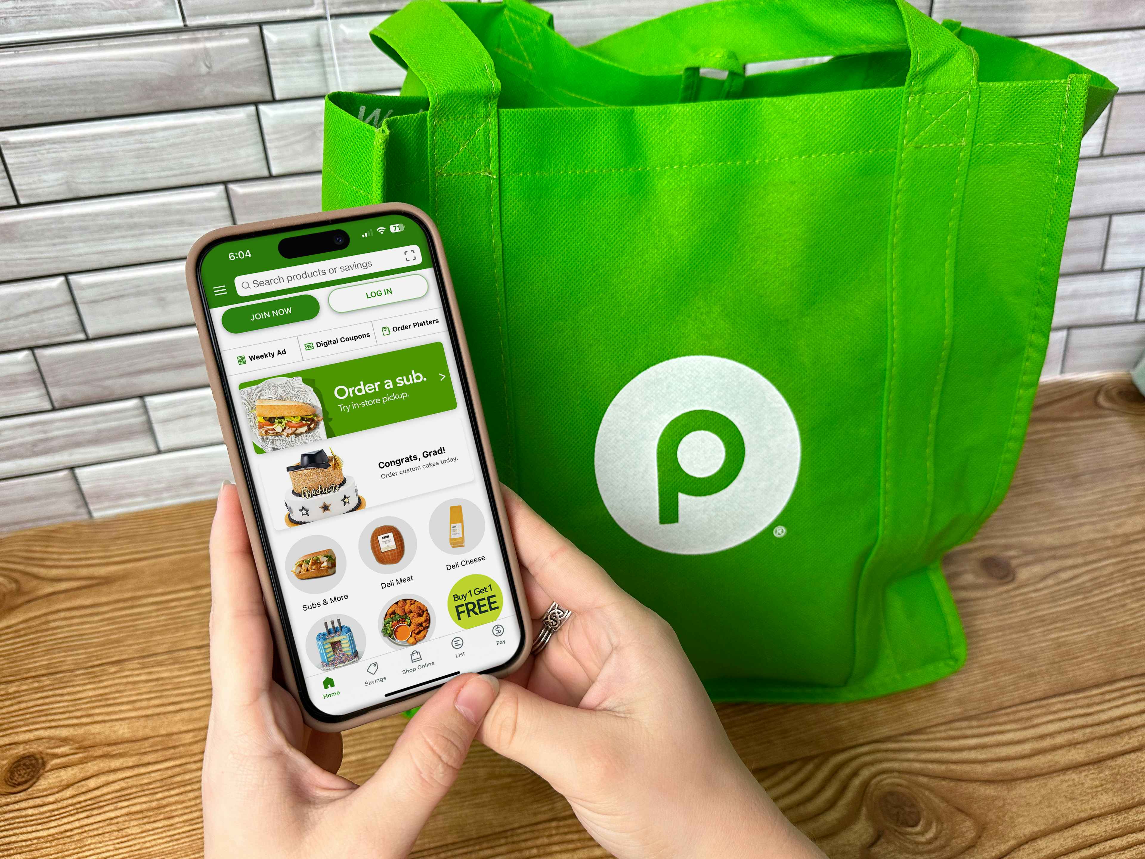 someone holding a phone displaying the Publix app next to a Publix reusable bag
