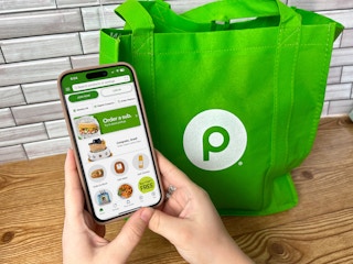 someone holding a phone displaying the Publix app next to a Publix reusable bag