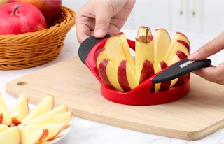 a person using a red apple slicer on a cutting board