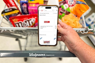 A person holding up an iphone 14 in front of a walgreens shopping cart