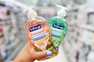 a woman holding up two bottles of Softsoap Hand Soap in the Walgreens store