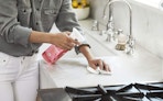 a person cleaning a kitchen sink count with a pink bottle of cleaner