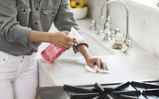 a person cleaning a kitchen sink count with a pink bottle of cleaner
