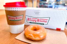 A Krispy Kreme donut and small coffee sitting on a table at the store