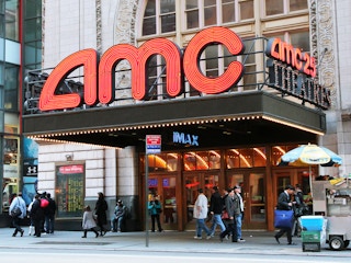 An AMC movie theater entrance with people walking by on the sidewalk.
