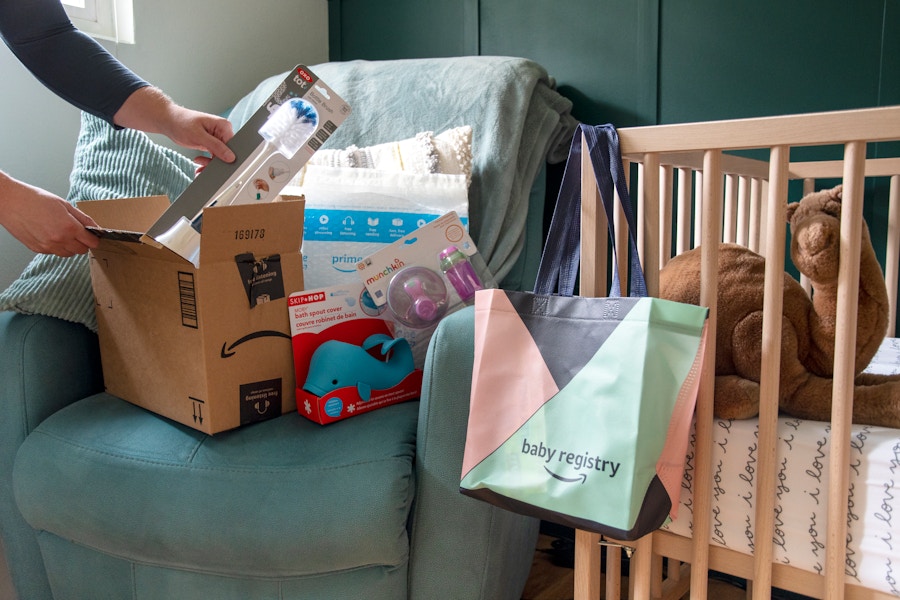 A person pulling baby products out of an amazon box. An amazon welcome bag is hanging on a crib near by