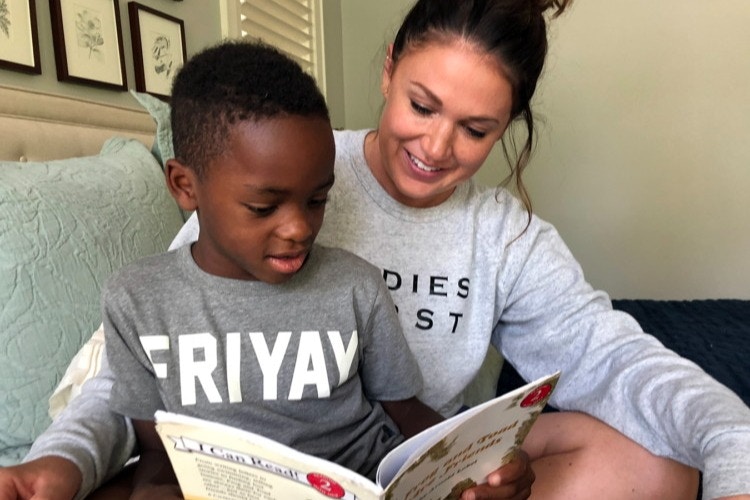 A woman sitting on a couch with a child sitting on her lap while they both read a children's book.