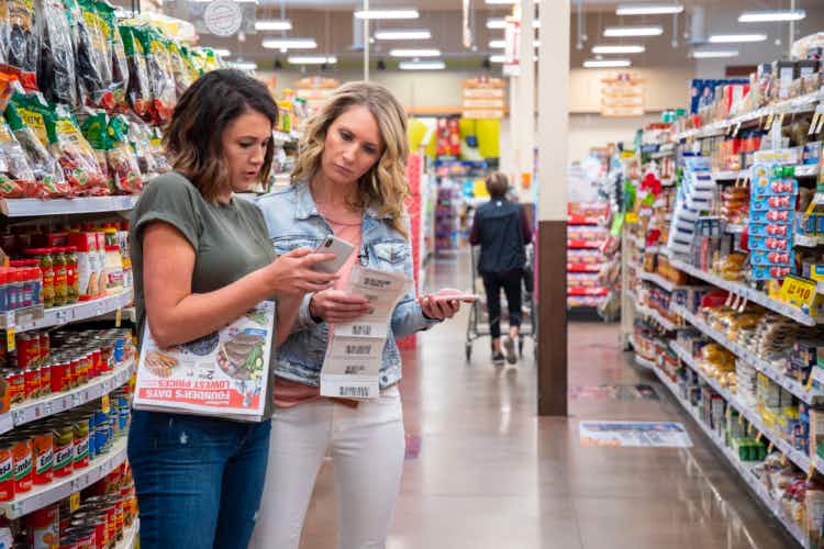 Two women looking at an app while holding a sales ad and coupons in a store