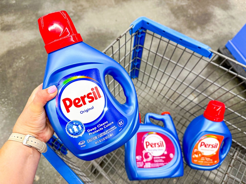 hand holding a bottle of persil liquid detergent with two others in walmart cart