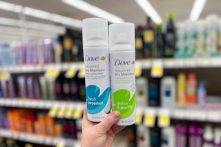 hand holding two cans of dry shampoo in front of store shelves in shampoo aisle