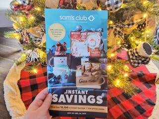 hand holding sam's club instant savings book in front of a christmas tree