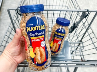 hand holding bottle of peanuts in front of shopping cart