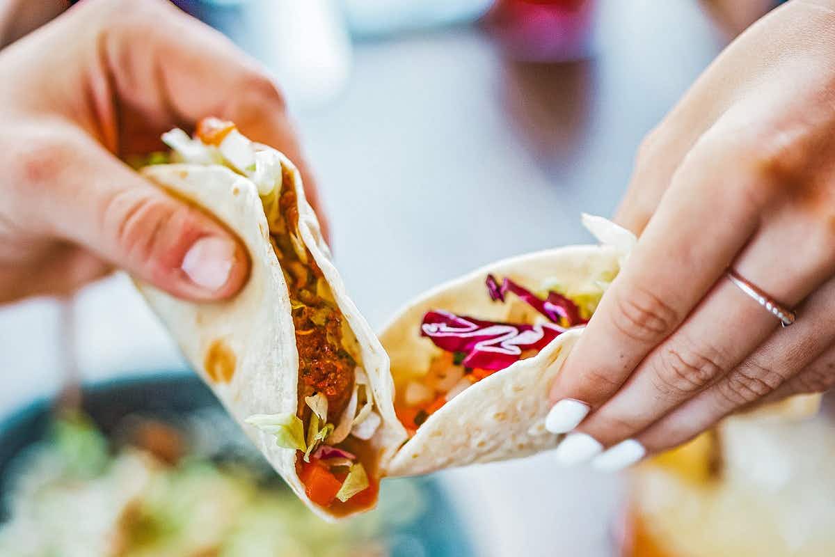 Two people holding a taco in their hands.