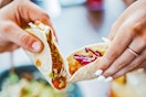 Two people holding a taco in one hand.