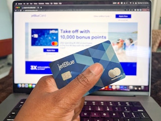 Hand holding a jetblue card infront of a laptop
