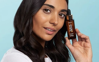 person holding a bottle of L'oreal sublime bronze drops near their face