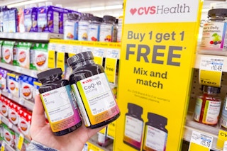 person holding 2 bottles of vitamins by a buy one, get one free sign