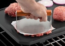 a burger being pressed out on a grill with a burger press