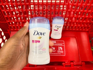 A hand holding Dove deodorant in front of a store cart.