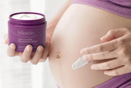 a pregnant woman holding a purple jar of stretch mark cream and applying it