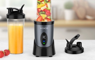 a blender full of fruit next to a cup with fruit juice 