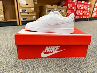 A Nike shoe sitting on top a Nike box sitting on the floor.