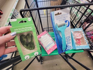 hand holding a jade gua sha massager over a cart with other skincare tools in it
