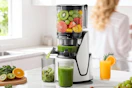 a juicer with fruit and veggies juicing in a cup