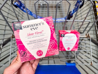 hand holding a box of Summer's Eve feminine wipes over another box in a Walmart cart