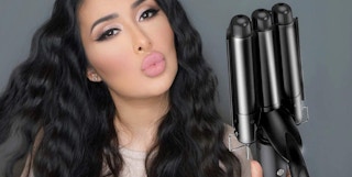 person holding a curling iron with long wavy black hair