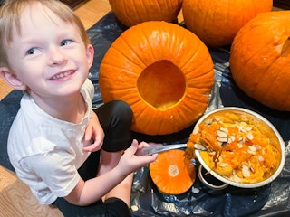 a little boy using a spoon to pull out pumpkin seeded and guts