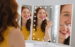 a person doing their makeup in a tri-fold mirror
