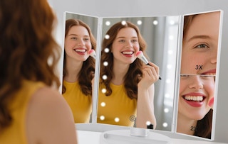 a person doing their makeup in a tri-fold mirror