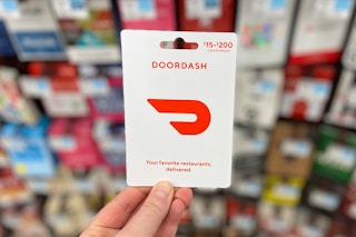 hand holding a doordash gift card in front of gift cards on store shelves