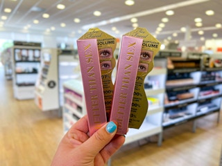 a hand holding two tubes of mascara in a store     