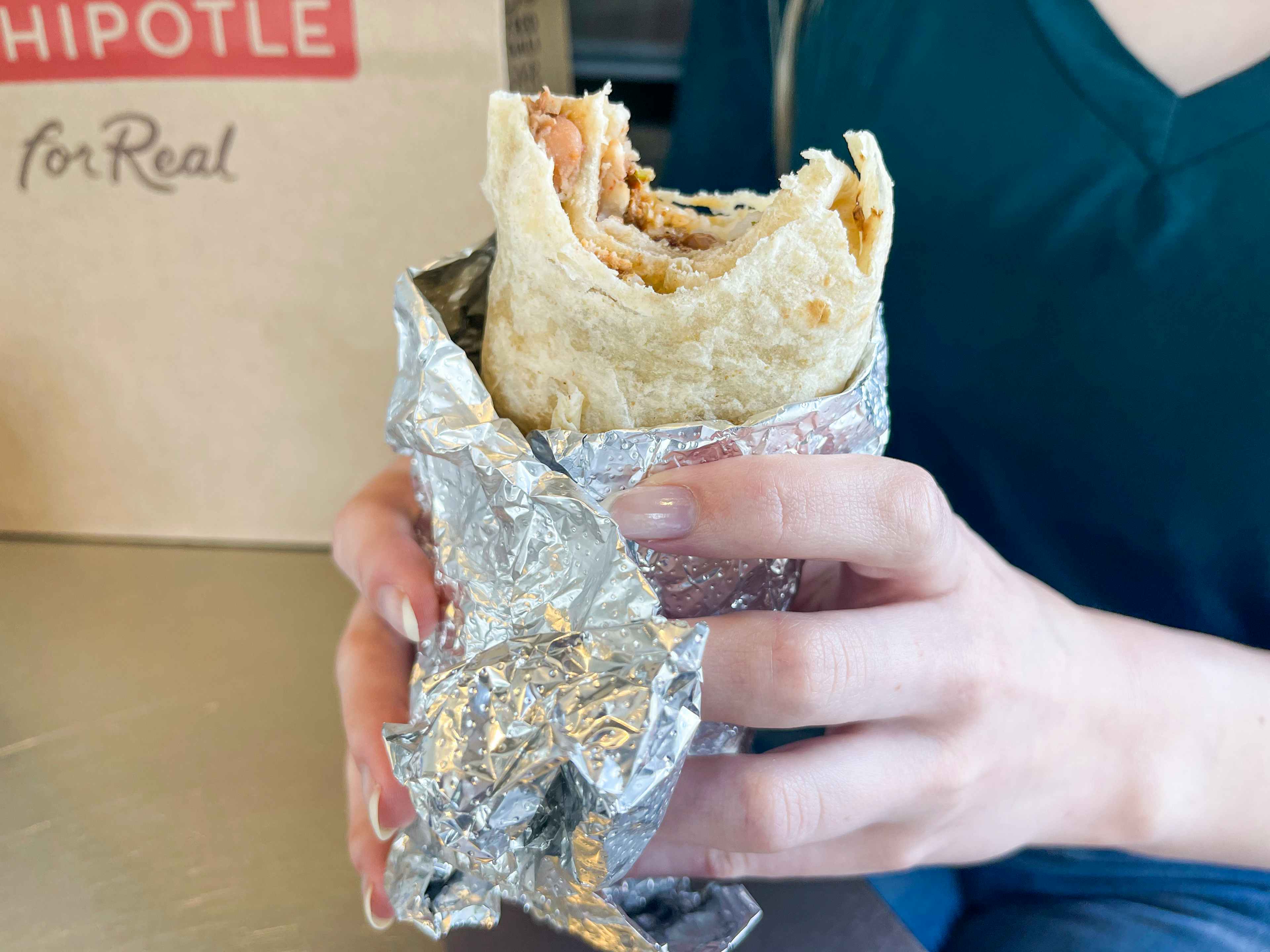 A person holding a burrito that has bitten into. The beans chicken and rice are visible inside.