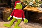 Lifestyle image of the Grinch Jumbo Plush seating near a Christmas tree