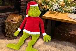 Lifestyle image of the Grinch Jumbo Plush seating near a Christmas tree