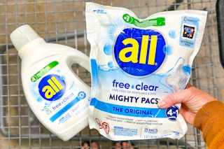 person holding a package of all mighty pacs over a cart with liquid all detergent in it