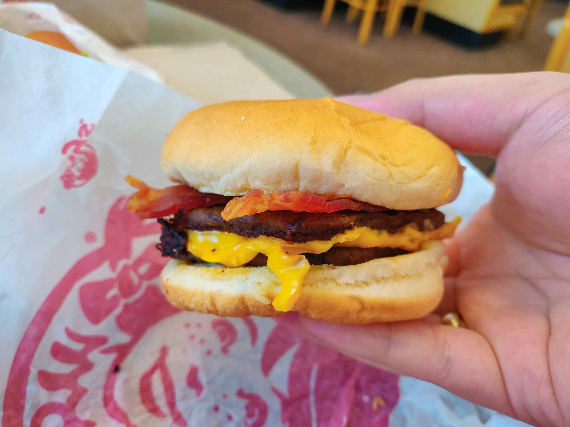A person's hand holding a Wendy's Bacon Double Stack burger above its paper wrapper.
