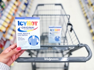 hand holding a box of icy hot arm, neck, and leg patches in front of shopping cart