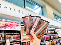 person holding 3 maybelline sky high mascaras by the display