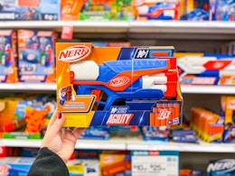 hand holding a nerf agility blaster in front of toys on a target shelf